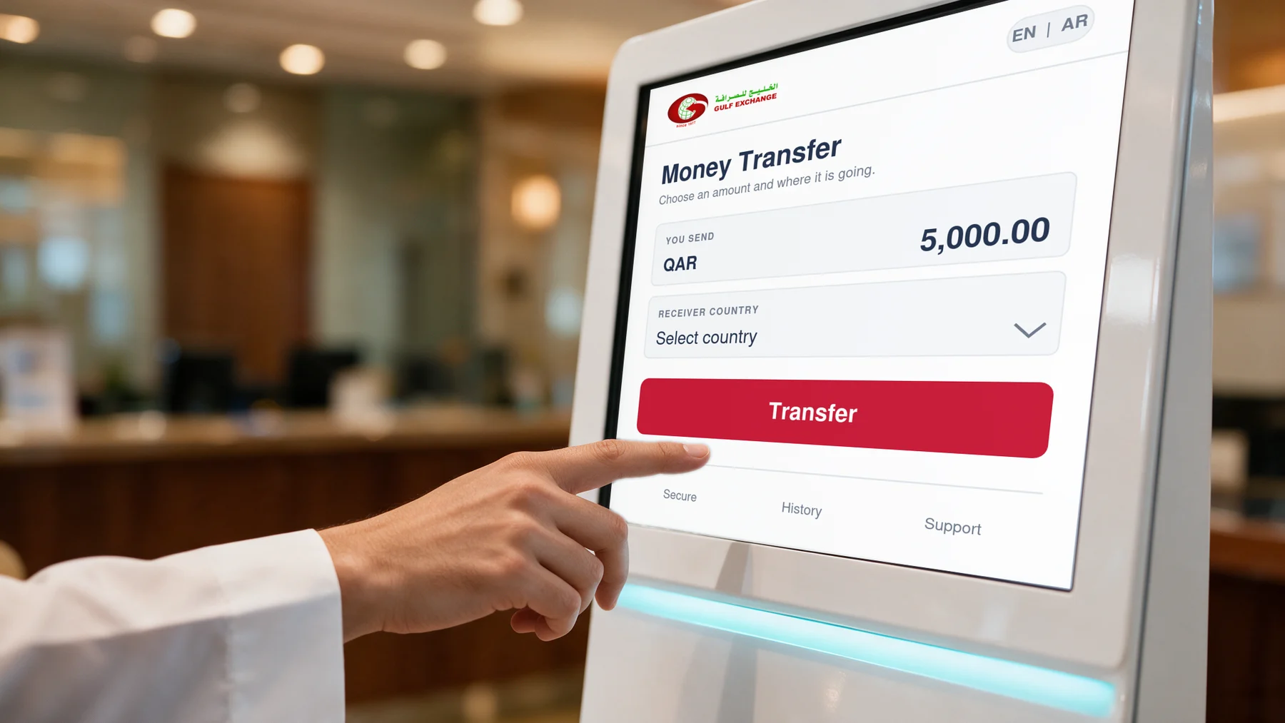 A customer in a white thobe touching the Transfer button on the money transfer screen of a Gulf Exchange self-service kiosk.